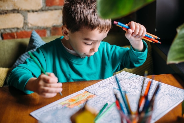 Portrait of a cute happy preschool boy at home or in a cafe draws