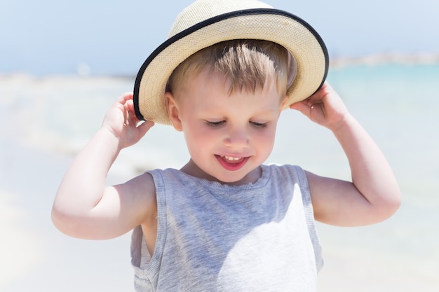 Portrait of cute kid boy on the beach in straw hat