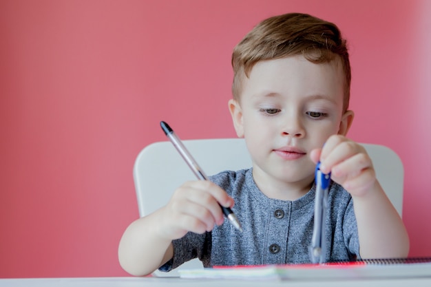 宿題を家で作るかわいい子供男の子の肖像画。屋内でカラフルな鉛筆で書く少し集中している子。