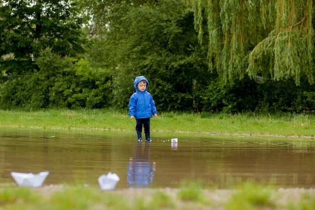 Portrait of cute kid boy playing with handmade ship kindergarten boy sailing a toy boat by the waters' edge in the park