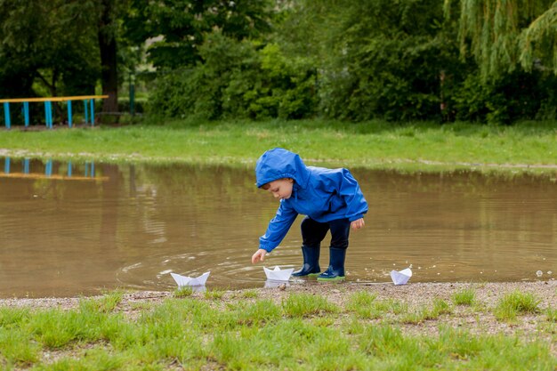 Portrait of cute kid boy playing with handmade ship. kindergarten boy sailing a toy boat by the waters' edge in the park