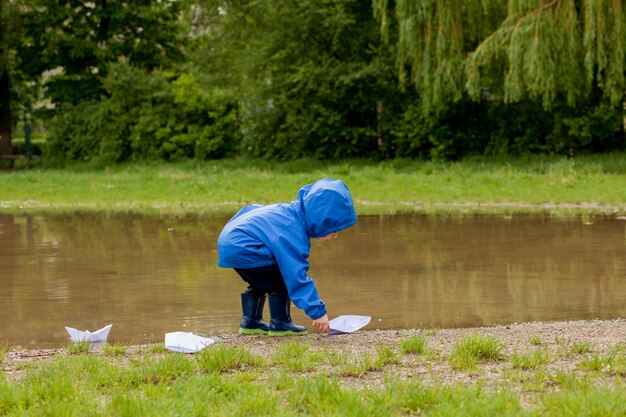 手作りの船で遊ぶかわいい男の子の肖像画。公園の水際でおもちゃのボートを航行する幼稚園の少年。