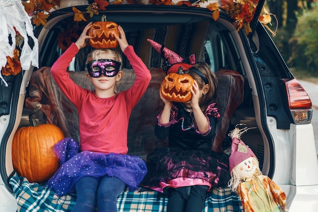 Portrait of cute kids holding pumpkin sitting in car trunk