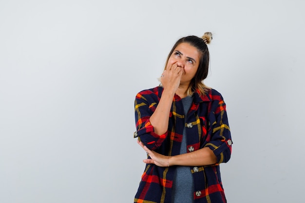 Portrait of cute lady biting nails, looking up in checked shirt and looking dreamy