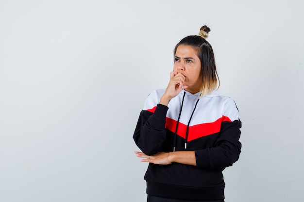 Portrait of cute lady keeping hand on chin, looking away in hoodie and looking thoughtful front view