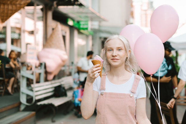 Ritratto di una signora carina che cammina per strada con gelato e palloncini