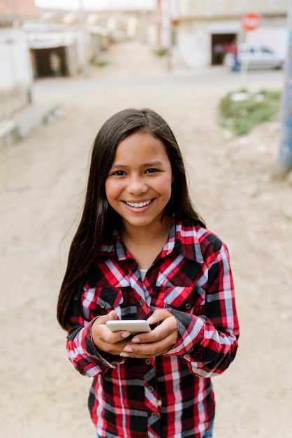 Portrait of cute latino girl using the mobile in shanty town. childhood concept.