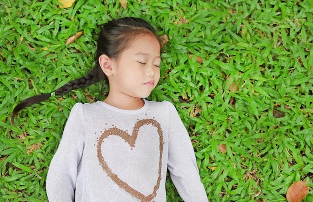 Portrait of cute little Asian child girl lying on green lawn.