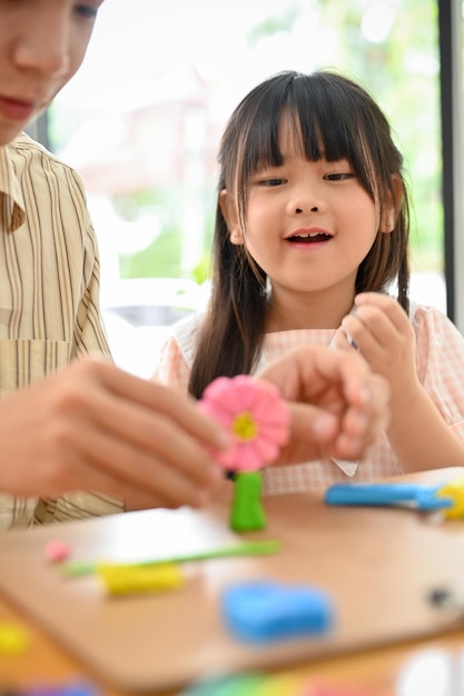 Ritratto piccola ragazza asiatica sveglia che gioca la pasta del gioco con il suo fratello che fa i fiori svegli