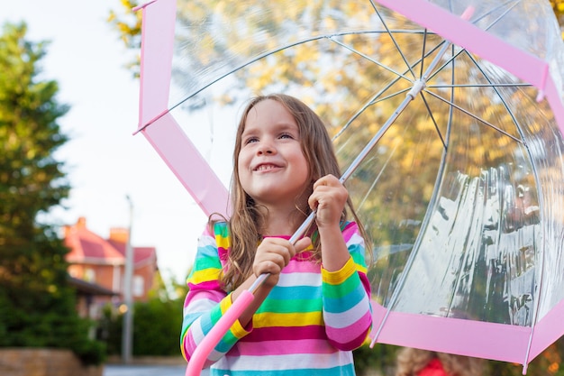 Portrait of a cute little baby girl walking near the house with an umbrella 