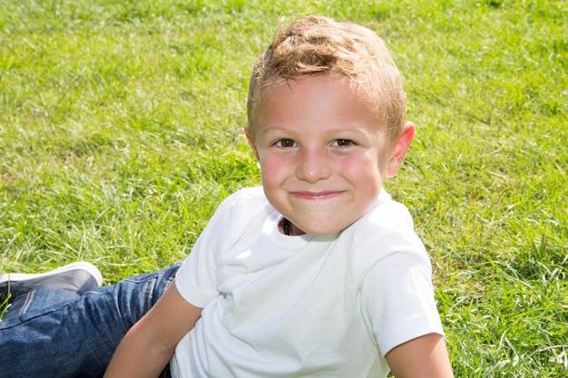 Portrait of cute little blonde boy lying on home garden grass park