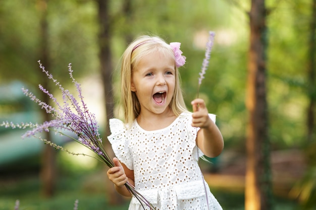 Portrait of cute little blonde girl with bouquet of lavender in summer park