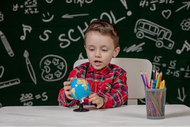 Portrait of cute little boy holding in hands small globe on blackboard