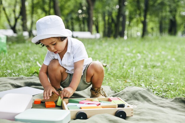 Portrait of cute little boy playing with toys in park while sitting on green grass and enjoying summ...