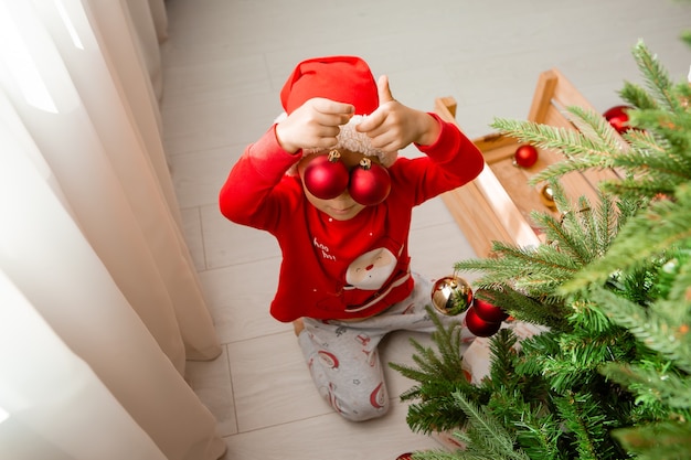 portrait of a cute little boy in red pajamas decorating a Christmas tree winter New years concept