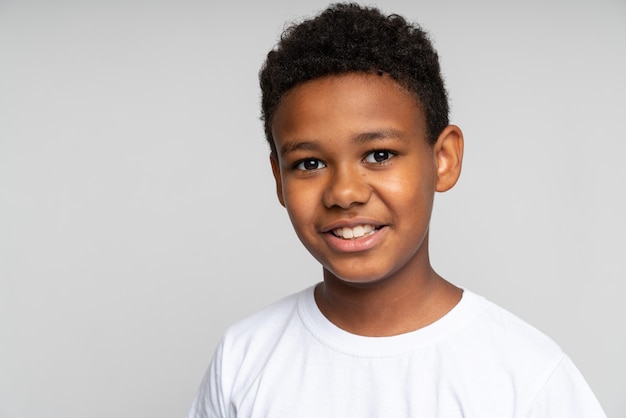 Portrait of cute little boy with stylish curly hairdo in white T-shirt standing, looking at camera with happy attentive face. Calm expression. Indoor studio shot isolated on white background