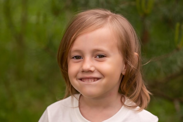 Portrait of cute little caucasian girl in casual closing in the forest against the background of grass summertime