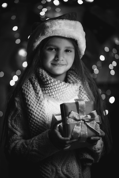 Ritratto di una bambina carina che tiene in mano una scatola regalo di natale incandescente