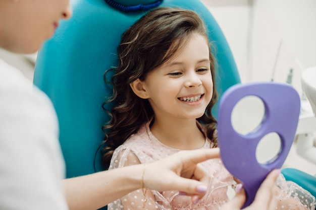 Ritratto di una bambina carina guardando i suoi denti dopo aver fatto un intervento chirurgico ai denti in una stomatologia pediatrica mentre era seduto nel sedile di stomatologia.