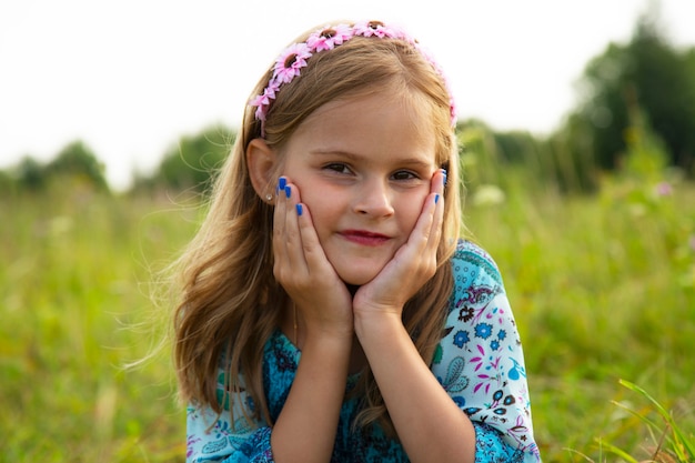 牧草地に横たわっているかわいい女の子の肖像画。巻き毛の茶色の髪の7-9歳の美しい少女。