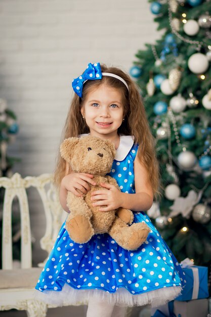 Portrait of a cute little girl near a Christmas tree. Posing with a teddy bear whom she was presented with a Christmas present for Christmas.