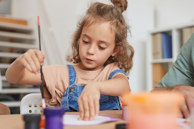 Ritratto di ragazza carina che dipinge immagini mentre ti godi la lezione di arte e artigianato a scuola o nel centro di sviluppo