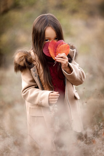 Portrait of cute little girl playing with autumn fallen leaves