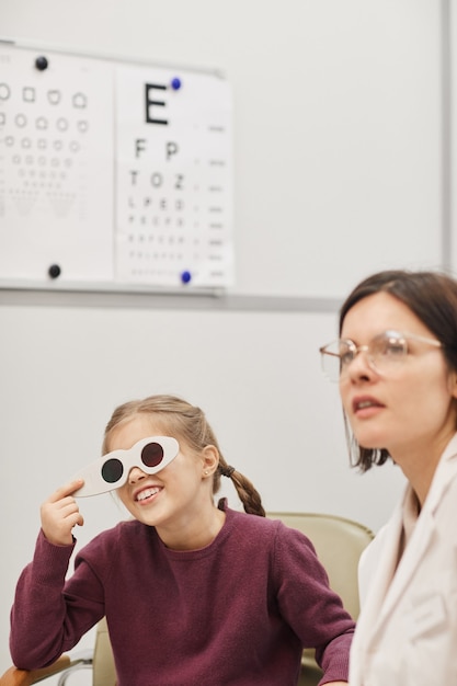 Photo portrait of cute little girl reading vision chart during eyesight test in pediatric ophthalmology clinic