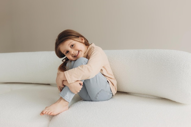 Portrait of a cute little girl sitting on the couch The smiling girl hugged her knees