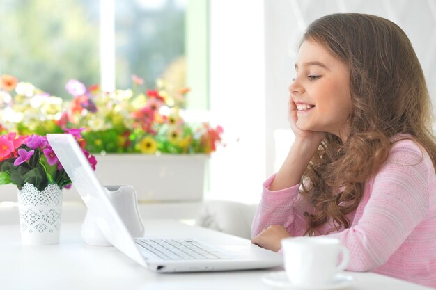 Portrait of cute little girl sitting at the table with laptop