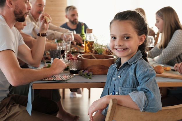 Portrait of cute little girl smiling while sitting on chair and having dinner with her big family