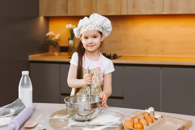 Портрет милой маленькой девочки, стоящей на современной кухне и готовящей тесто