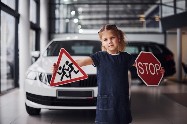 Portrait of cute little girl that holds road signs in hands in automobile salon.
