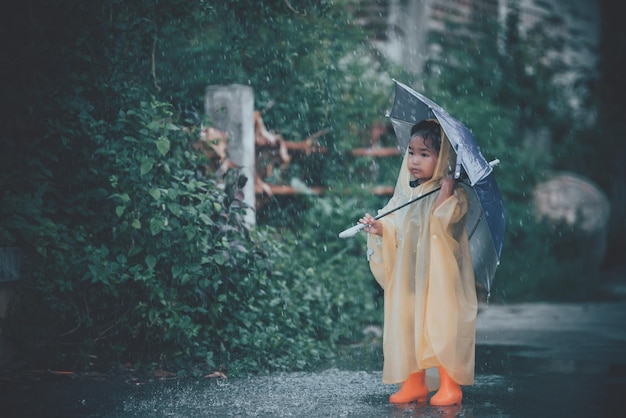 Portrait of cute little girl wearing raincoat and holding umbrella on the rainingThailand people