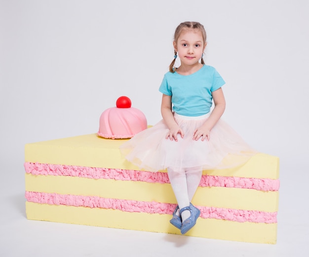 Portrait of cute little girl with big cake over white background