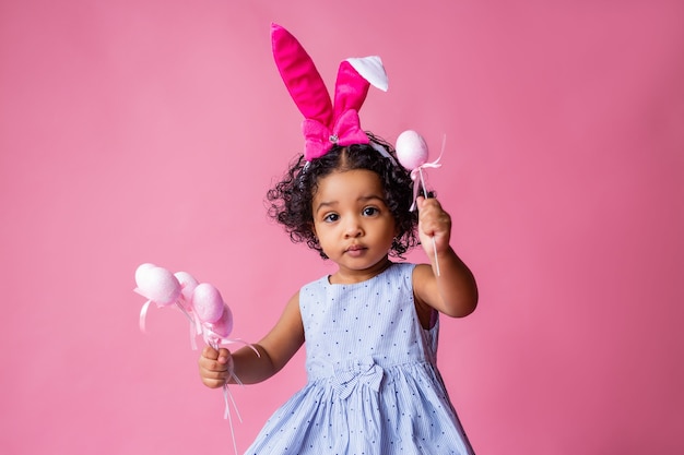 portrait of a cute little girl with Easter bunny ears on her head holding Easter eggs. studio, pink background