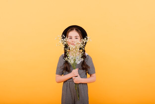 Portrait of cute little girl with flower bouquet in the studio on yellow background.