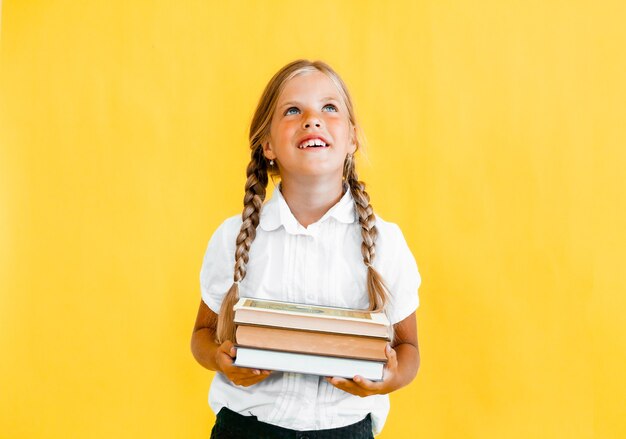 Портрет милой маленькой девочки на желтом фоне. Школьница смотрит в камеру,