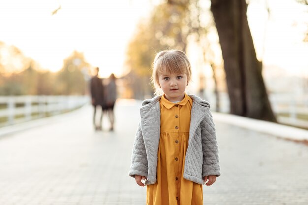 Portrait of Cute little girl in yellow dress outdoors in autumn park