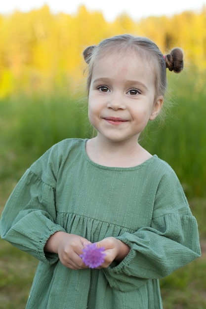 Portrait of a cute little happy girl with blooming lupine flowers in a field of flowers nature in the open air The concept of A child in nature Childhood Summer holidays holidays