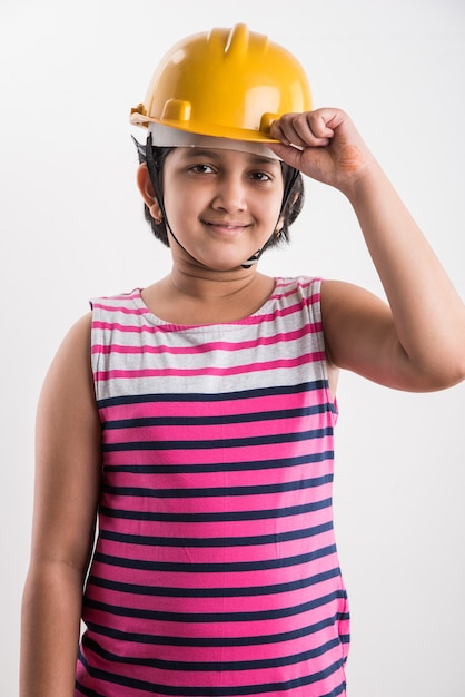 Portrait of cute little indian girl in yellow hard hat holding paper roll, Standing isolated over white background
