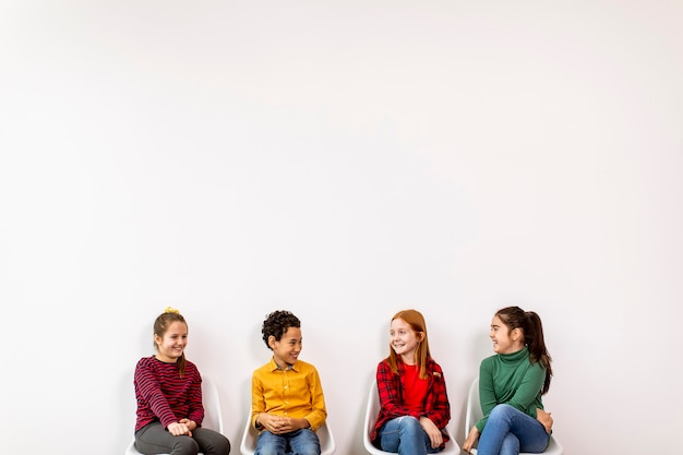 Portrait of cute little kids in jeans  sitting in chairs against the white wall