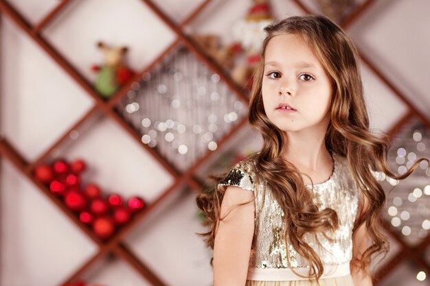 Portrait of cute long-haired little girl in dress on background of christmas lights