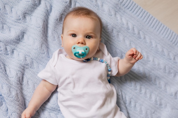 Photo portrait of cute newborn baby with a pacifier in his mouth lying on his back on blue knitted blanket. breastfeeding. concept of a happy childhood and motherhood. a healthy child. high quality photo