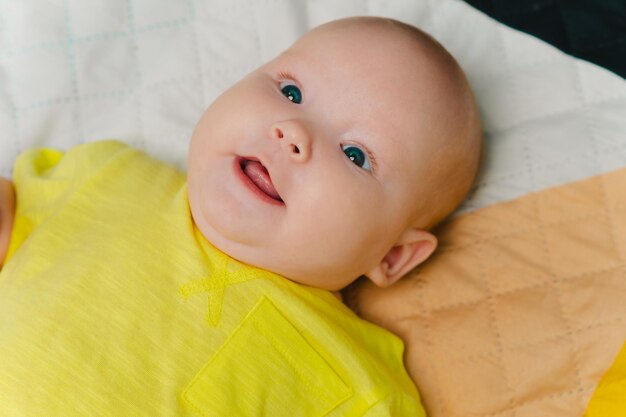 Portrait of a cute newborn girl lying on a bed in a yellow Tshirt