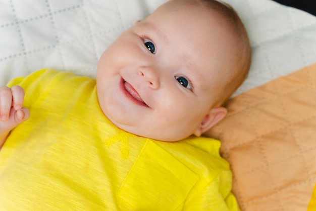 Portrait of a cute newborn girl lying on a bed in a yellow Tshirt