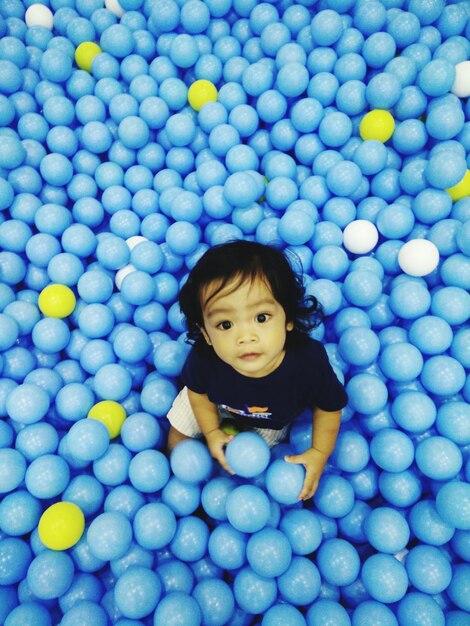 Photo portrait of cute playful boy amidst blue balls