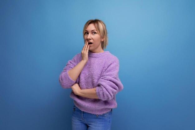 Portrait of a cute pleasant blond young woman in a lavender sweater shocked on a bright plain