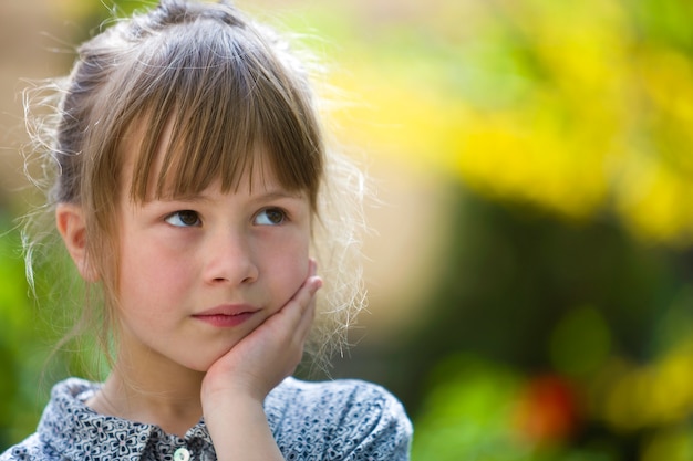 Portrait of cute pretty thoughtful child girl outdoors on blurred sunny colorful bright