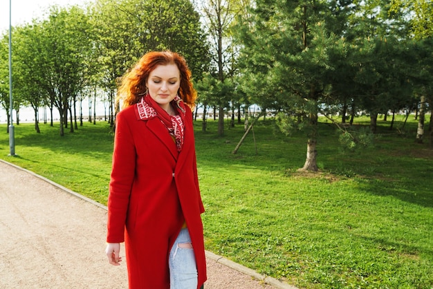 Portrait of cute redhaired woman in a red coat in the park